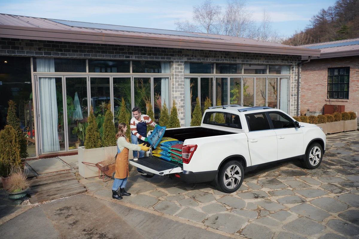 Bags of soil being loaded into the tray of a white KGM Musso Grand outside a garden centre