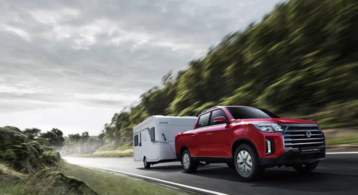 An Indian Red KGM Musso Grand towing a caravan on a country road