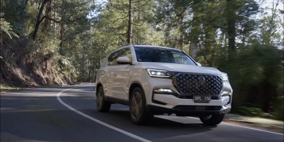 A white KGM Rexton on a winding forest road