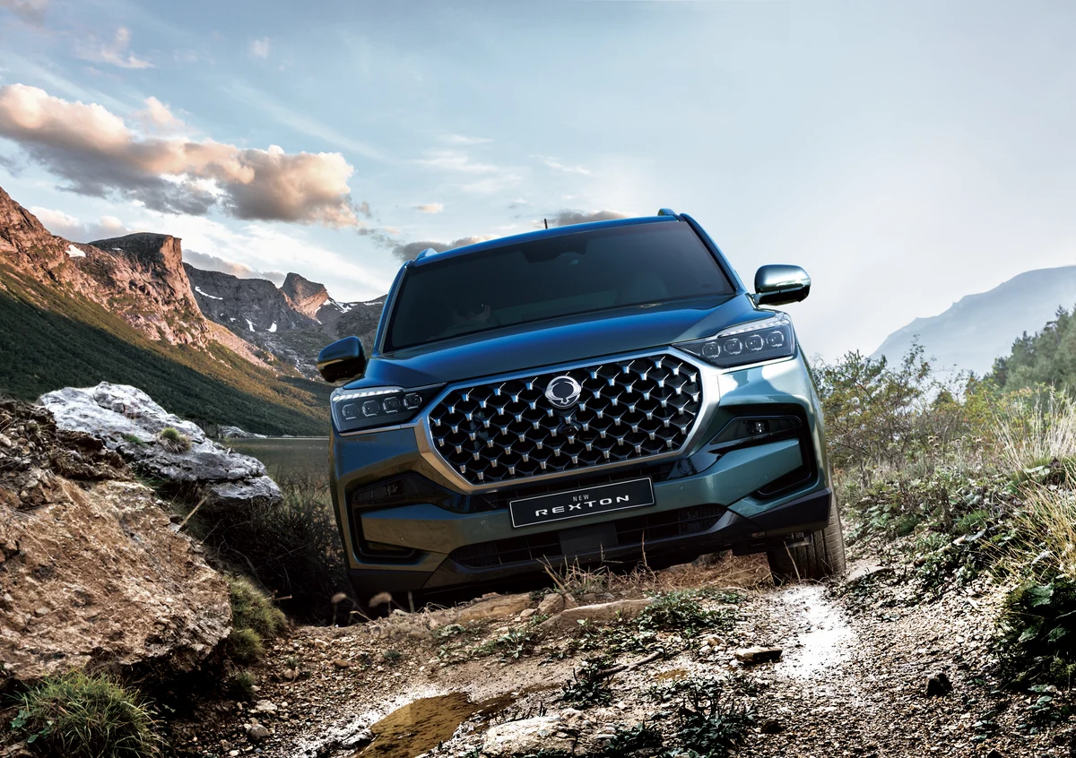 A blue-grey KGM Rexton climbing over rocks on a mountain track