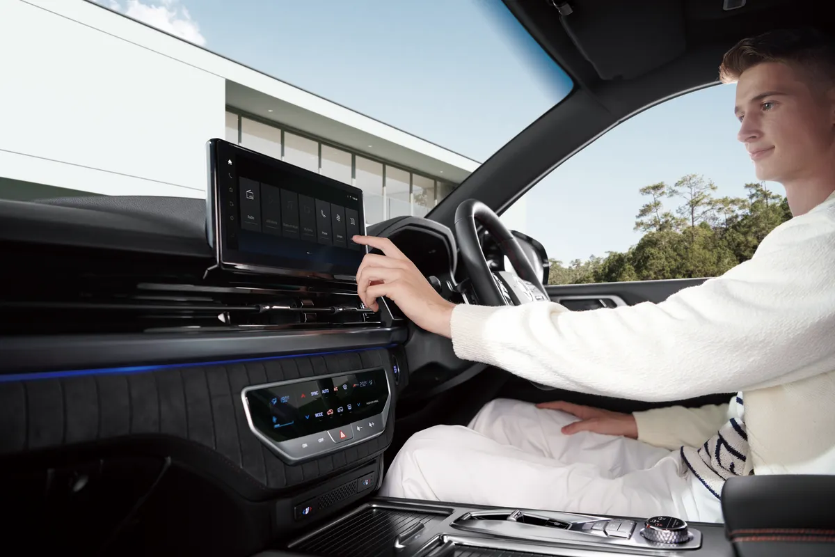 A driver reaching for the touchscreen of a KGM Rexton